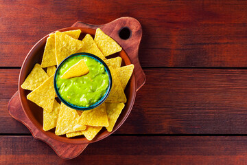 Bowl with guacamole and nachos on wooden boards. Mexican guacamole dip and tortilla chips in a clay plate. Copy space. Top view