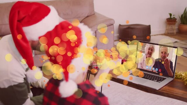 Animation of spots over caucasian father and son in santa hats on laptop video call at christmas