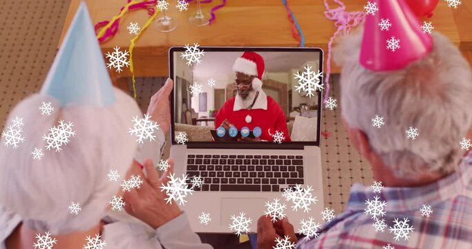 Animation of snow falling text over senior caucasian couple on laptop video call at christmas