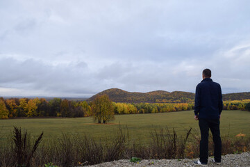 Fototapeta na wymiar A man stands on the road and looks towards the mountains covered with forest with colorful autumn leaves