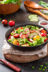 Spring vegetable salad with olive oil and sumac in a black bowl on a dark background. Salad of radishes, cucumbers, tomatoes, lettuce, sumac, and olive oil. Vegan or diet food. Healthy lunch.