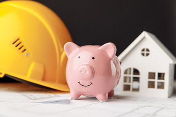 Building costs concept. Yellow safety helmet and pink piggy bank with drawings and model of house close-up