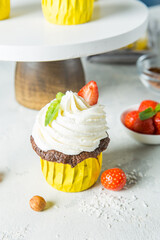 Chocolate cupcake with white cream and strawberry slices on a light background