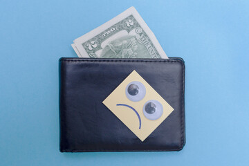 Two dollars are in the wallet. Sad smiley looks at the wallet. Blue background. Bankrupt. Money is tight. Importance of savings. Financial aid concept.