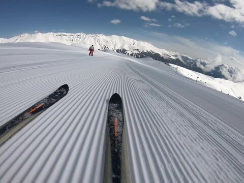 Close-up skiing glides down the undulating snowy slope to mountains on horizon