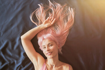 Pretty woman with long loose pink hair and silver jewellery lies on soft comfortable bed
