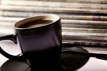 Cup of coffee and newspapers pile on the table.