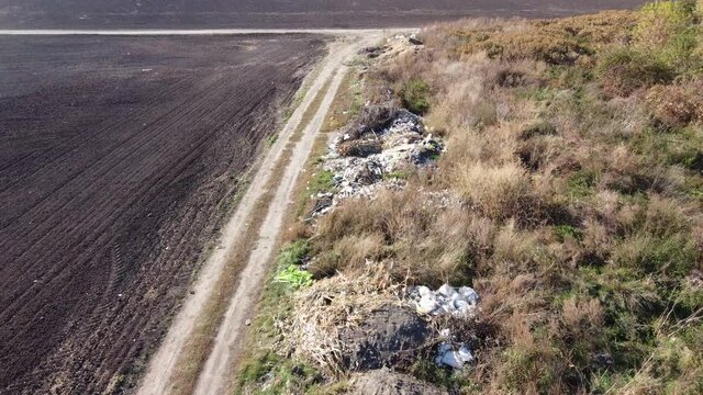 Illegal dumping of waste in the middle of nature near greenery and fields. Lots of hazardous waste from rubber, plastic, cement, metal