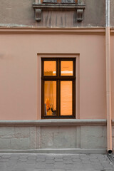 street exterior view with beige wall and window frame with lamp yellow light from inside vertical outdoor photo