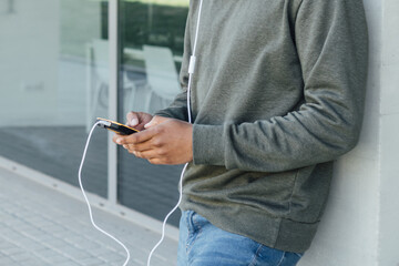 Close up view of a man using his mobile phone with earphones while standing outdoors on the street. Urban concept.