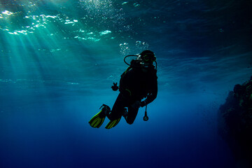 Woman scuba diver swimming in deep blue with sun rays