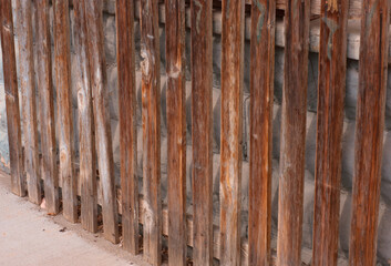 Double wall of wood fencing placed in front of cement blocks. This is an  old structure and photo is taken on an angle so part of sidewalk is visible.