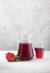 Jug of pomegranate juice with pieces of pomegranate fruits on a gray background