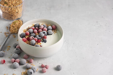 Bowl of homemade yogurt with granola and frozen berries covered with hoarfrost on gray background