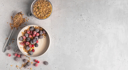 Obraz na płótnie Canvas Bowl of homemade yogurt with granola and frozen berries covered with hoarfrost on gray background, flat lay