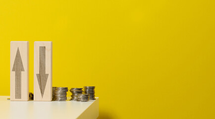 two wooden bars with arrows up and down on the table with coins, yellow background. Falls and increases in prices for utilities