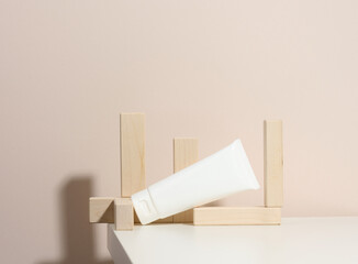 empty white plastic tubes for cosmetics on a beige background with wooden blocks. Packaging for cream, gel, serum, advertising and product promotion, mock up