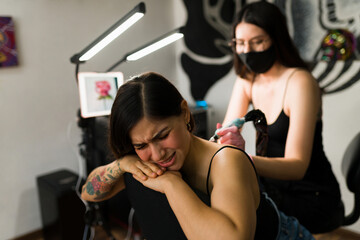 Distressed woman suffering while getting a tattoo
