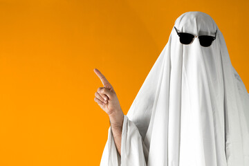 Person in Halloween costume of ghost with sunglasses points away - obrazy, fototapety, plakaty