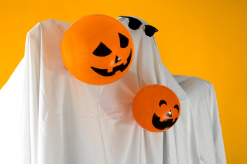 Person in Halloween costume of ghost with sunglasses and Jack-o'-lantern balloons dancing