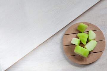Pieces of chayote cut on a small uncooked wooden board and white wooden background. View from...