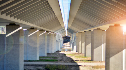Sunlight penetrates under overpass. Highway overpass bridge concrete structure with columns.