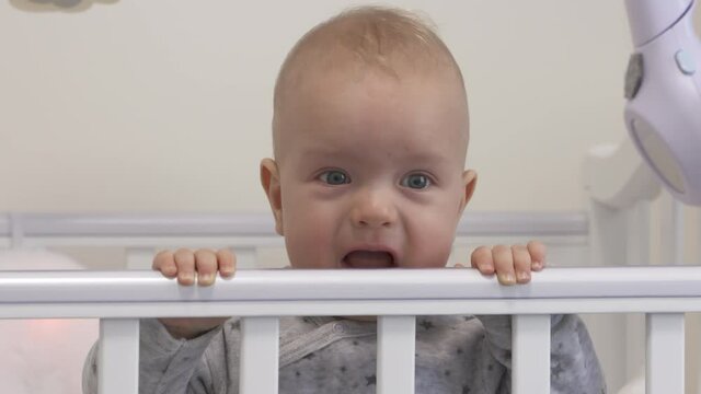 Baby sitting in infant bed, cute 7 months old baby boy playing in white rocking cradle at home. High quality 4k footage