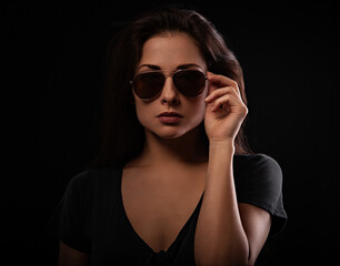 Fashionable chic female model front face in fashion sun glasses holding the hand on black background. Closeup