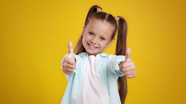 Like and approval. Studio portrait of cute little girl with two ponytails gesturing thumbs up with hands and smiling