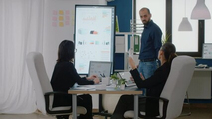 Man pointing at television with chart presentation for project planning while businesswomen listening to ideas for marketing strategy at meeting. Workmates with research development