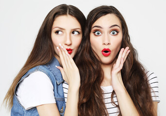 Portrait of two happy young women sharing secrets isolated over white background