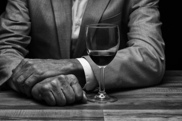 Closeup of a man seated at a table with a glass of red wine in front of his folded arms. Person is unrecognizable.