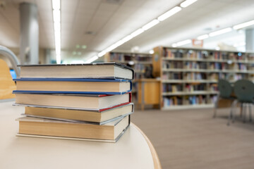 Stack of books on table against bookshelf at library for education, literature or wisdom concept © Kenishirotie