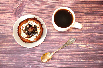 A saucer with chocolate sponge cake, a cup of black coffee and a vintage spoon on a wooden table.