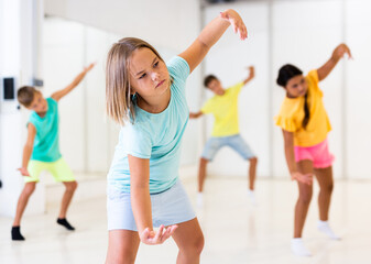 Young girl and her friends performing modern dance in studio during rehearsal.