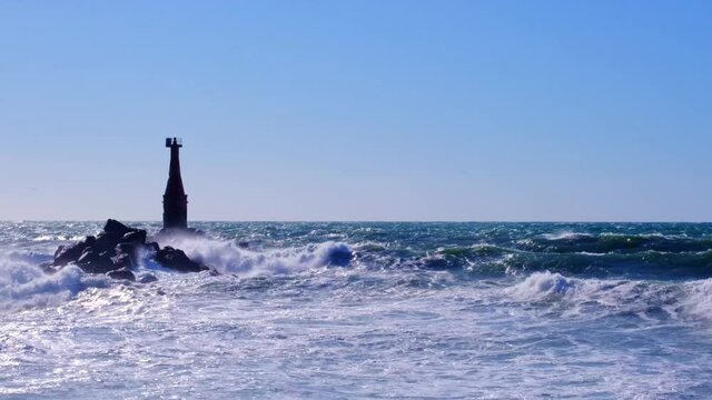 Storm at sea. Waves beat against the old lighthouse and rocks, forming splashes and foam.