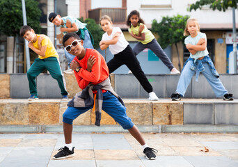 Cheerful preteen boys and girls breakdancers dancing on city street on summer day.