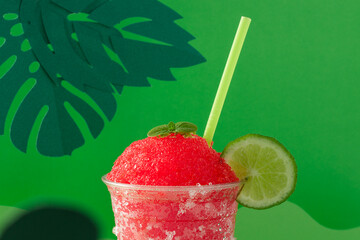 Strawberry and lemon slush in compostable glass on green background and green straw.