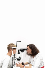 Attentive ophthalmologist examines a patient of a teenage boy with a slit lamp in an ophthalmology clinic. Side view. Free space for text