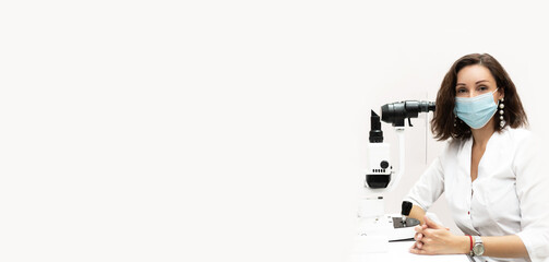 Banner portrait of a female optometrist doctor in a medical mask. Ophthalmology clinic, slit lamp....