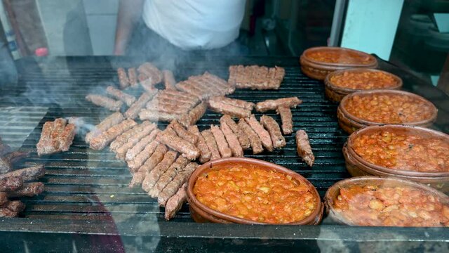 Cevapcici, cevapi on the grill. Balkans traditional food. Grilled dish of minced meat and vegetables. Grilled tasty meat on the barbecue. Chef is preparing delicious food. Cooked beans in pot.