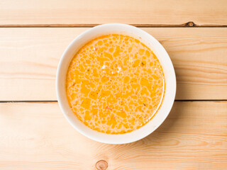 Cheese soup in a white round plate on a wooden background. View from above