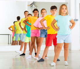 Naklejka premium Group of focused tween children standing akimbo in row one by one, learning movements of folk dance in choreography lesson