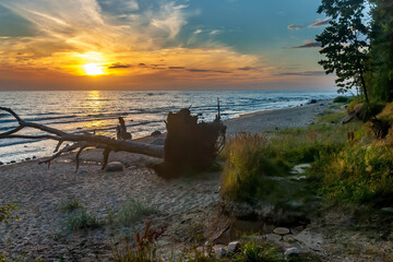 Fototapeta na wymiar Coastal landscape with sandy beach of the Baltic Sea and falling wooden snag at colorful sunset