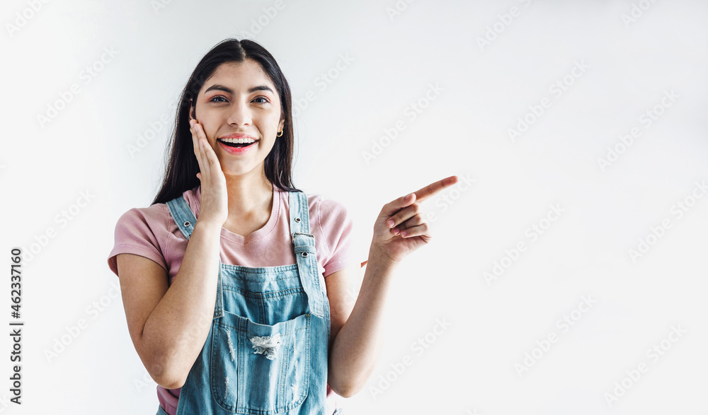 Wall mural young latin woman pointing at copy space looks in camera in latin america