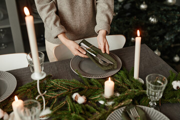 Closeup of unrecognizable woman setting up dining table for Christmas decorated with fir branches...