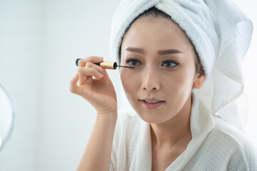 Beautiful girl in bathrobe and turban towel on her head makes herself a makeup in front of mirror, women lifestyle