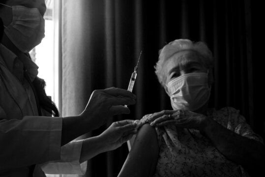 Doctor giving injection coronavirus vaccine to the elderly patient, general practitioner visiting her at home, elderly health care concept, selective focus, Black and white image