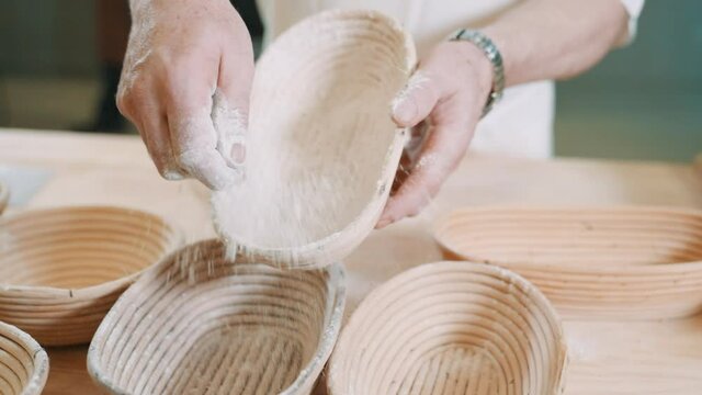 Artisan baker dusting flour on rattan banneton basket, making bread using traditional techniques