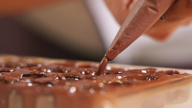 Chocolatier squeezing chocolate into praline mold, handmade fine chocolate praline production, close up